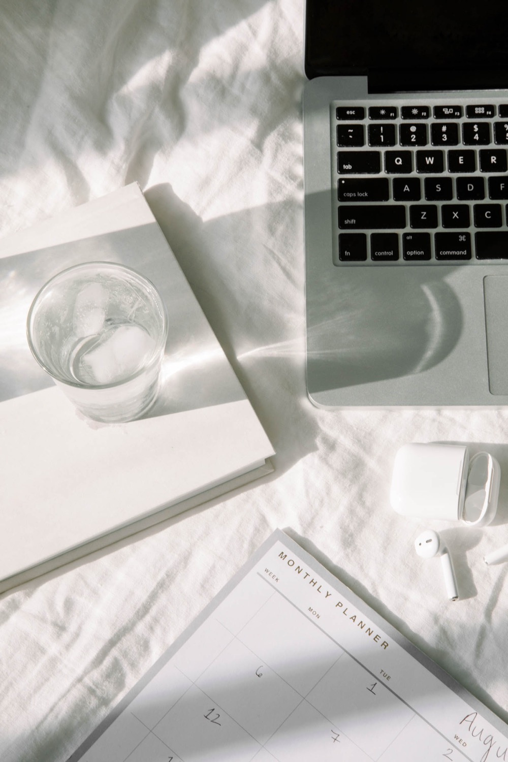 A laptop, notebook and monthly planner laid out on white linen