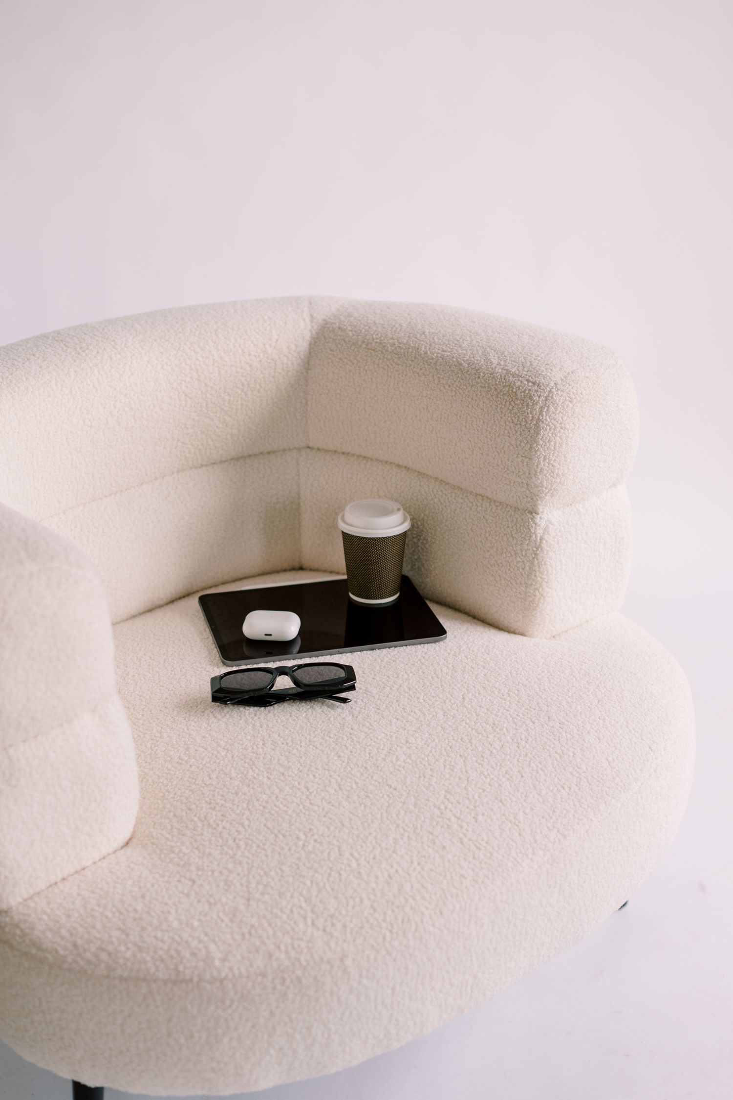 A cream boucle chair with a coffee and sunglasses on a tray