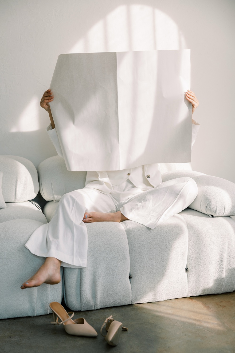 A woman on a sofa holding up a large blank sheet of paper
